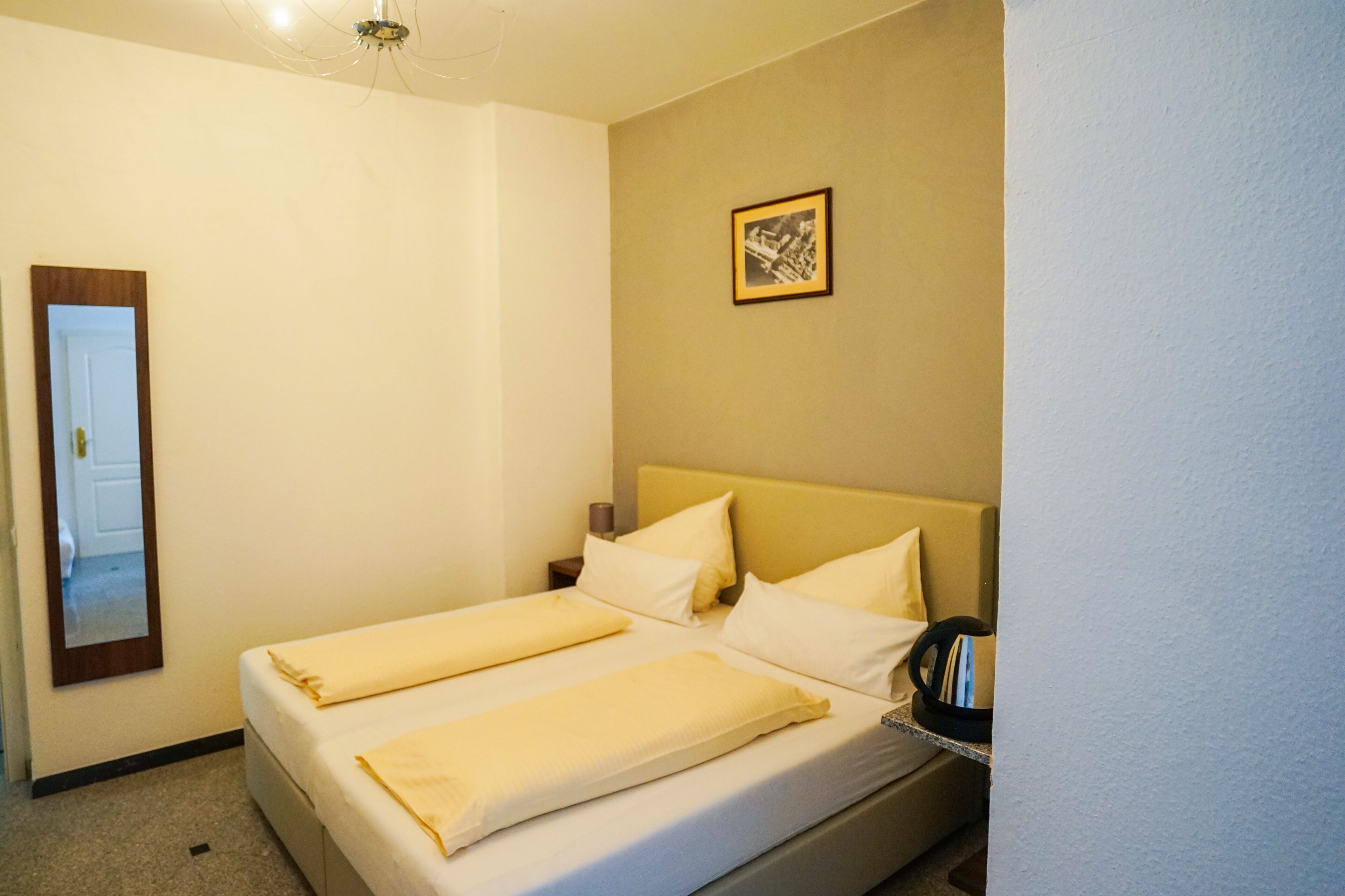 Ein Hotelzimmer mit einem Bett, einem Nachttisch, einer Lampe und einem gerahmten Bild an der Wand.