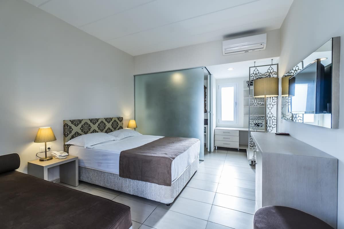 A modern hotel room with a bed, bedside tables, a desk, and a mirror.