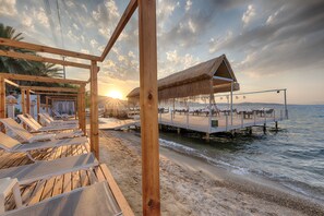 A wooden beach structure with lounge chairs and a thatched roof dining area overlooking the sea. - Babana Hotel (Bodrum)
