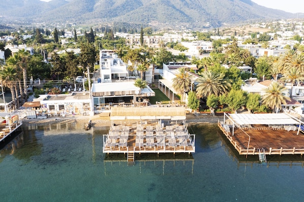 A waterfront property with a dock, lounge area, and a building with a thatched roof. - Babana Hotel (Bodrum)