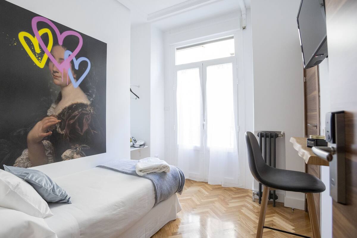 Un dormitorio con cama, una silla, un radiador y una ventana.