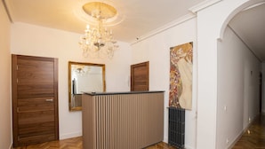 A hallway with a wooden floor, a reception desk, a chandelier, and a large mirror. - Hispano Boutique Gran Vía (Madrid)