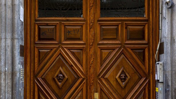 A wooden double door with intricate carvings and a brass handle. - Hispano Boutique Gran Vía (Madrid)