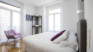 A modern bedroom with a large bed, a chair, and a TV mounted on the wall. - Hispano Boutique Gran Vía (Madrid)