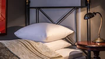 A neatly made bed with a white pillow and a patterned blanket, a round table with a lamp, and a sunburst mirror on the wall.