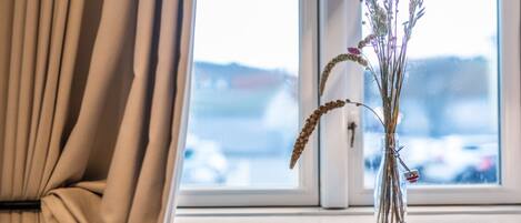 Une fenêtre donnant sur un paysage enneigé, un vase contenant des fleurs séchées et un rideau.