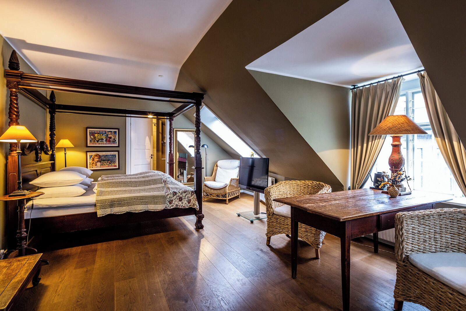 A four-poster bed, a television, wicker furniture, and a view of the city through large windows.