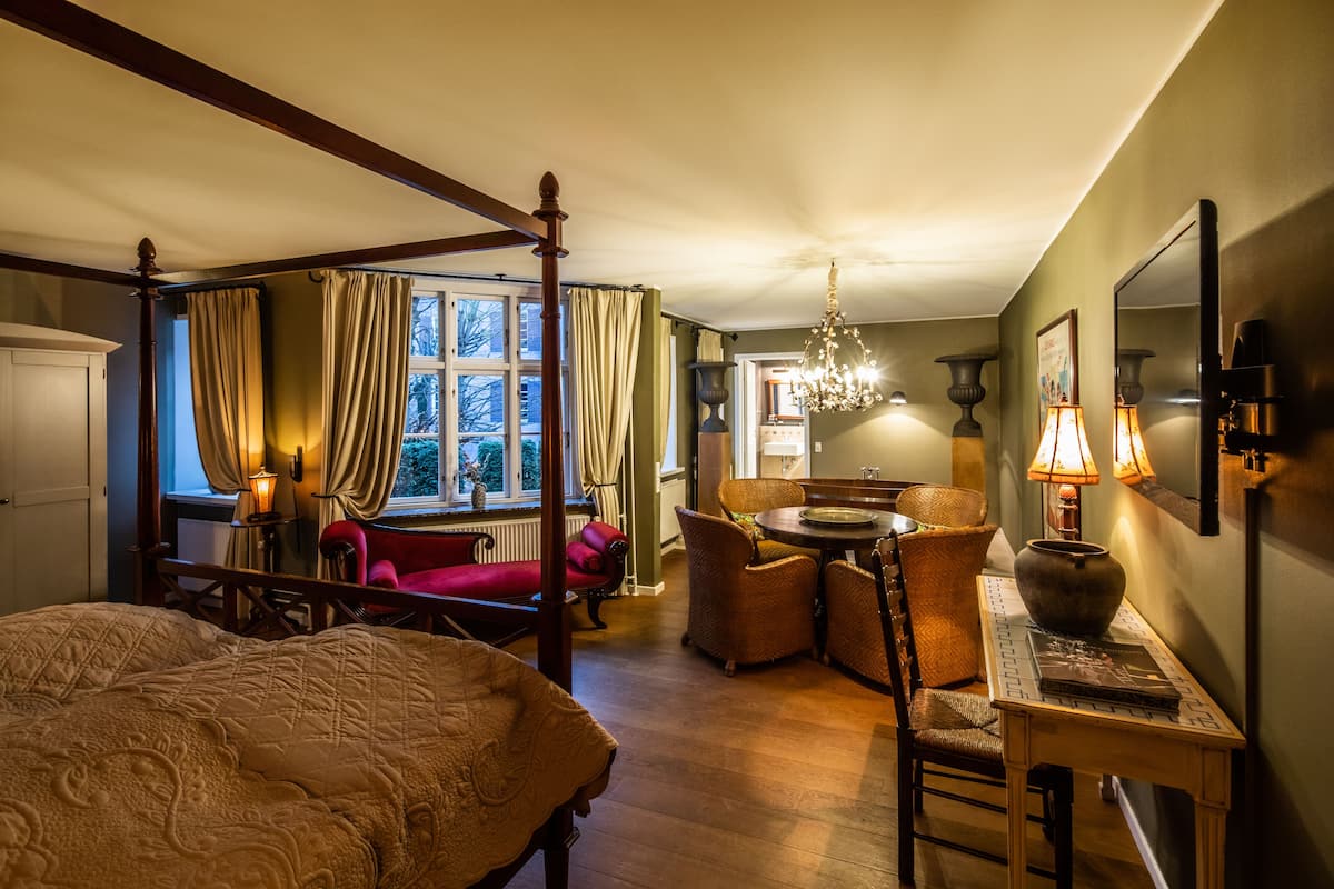 A four-poster bed, a dining table with chairs, and a chandelier in a hotel room.