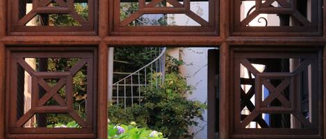 A wrought iron gate with geometric patterns, a metal staircase, and lush greenery.