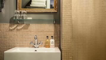 Un baño con un lavamanos blanco, dos botellas de loción y un espejo con marco dorado.
