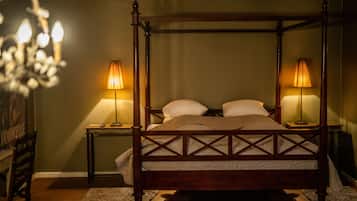 Una cama con dosel de madera, dos mesitas de noche con lámparas, y un candelabro al fondo.