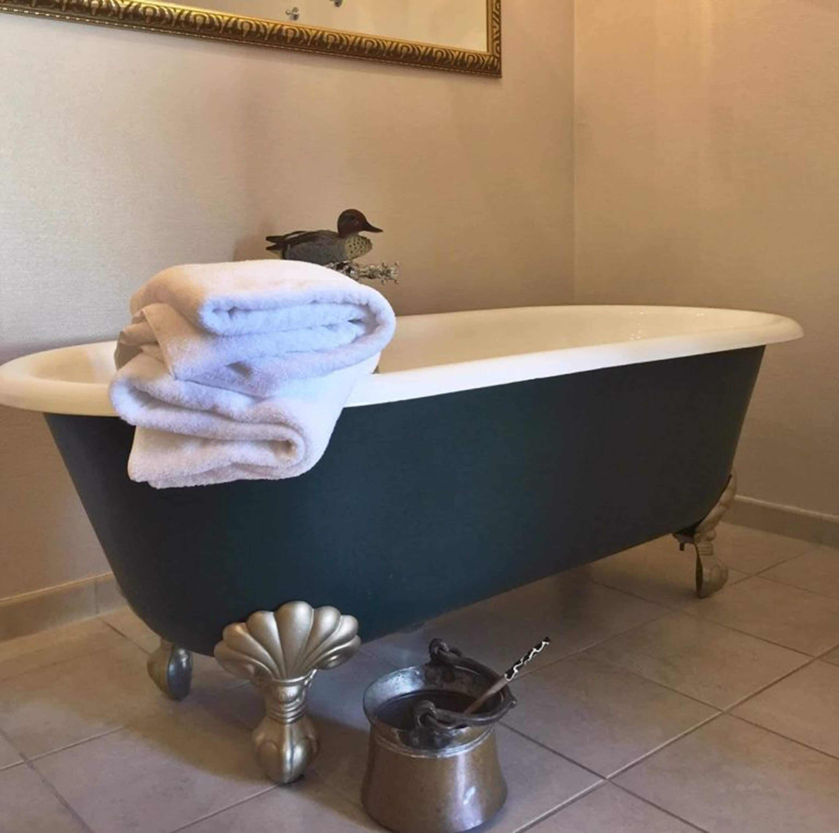 A clawfoot bathtub with a white interior, a folded white towel on the edge, a decorative shell, and a metal bucket with a hook on the floor.