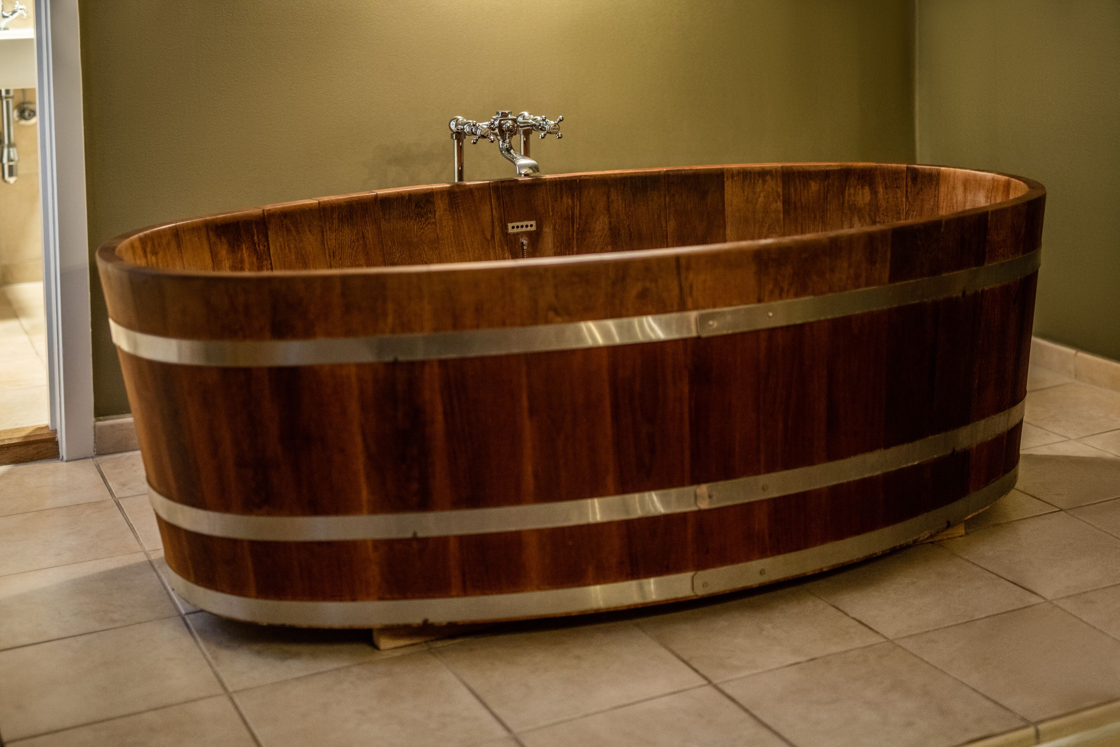 A wooden bathtub with metal bands, a faucet, and a tiled floor.