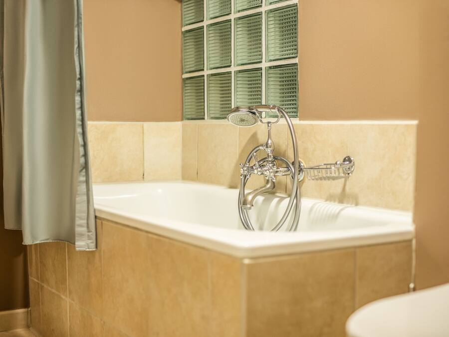 A bathroom with a bathtub, a shower, and a window with green shutters.