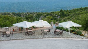 A patio with outdoor seating and umbrellas overlooking a mountainous landscape. - Balkoni Zagoriou (Zagori)