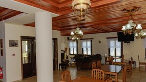 A spacious dining area with wooden tables and chairs, a sofa, and a television. - Balkoni Zagoriou (Zagori)
