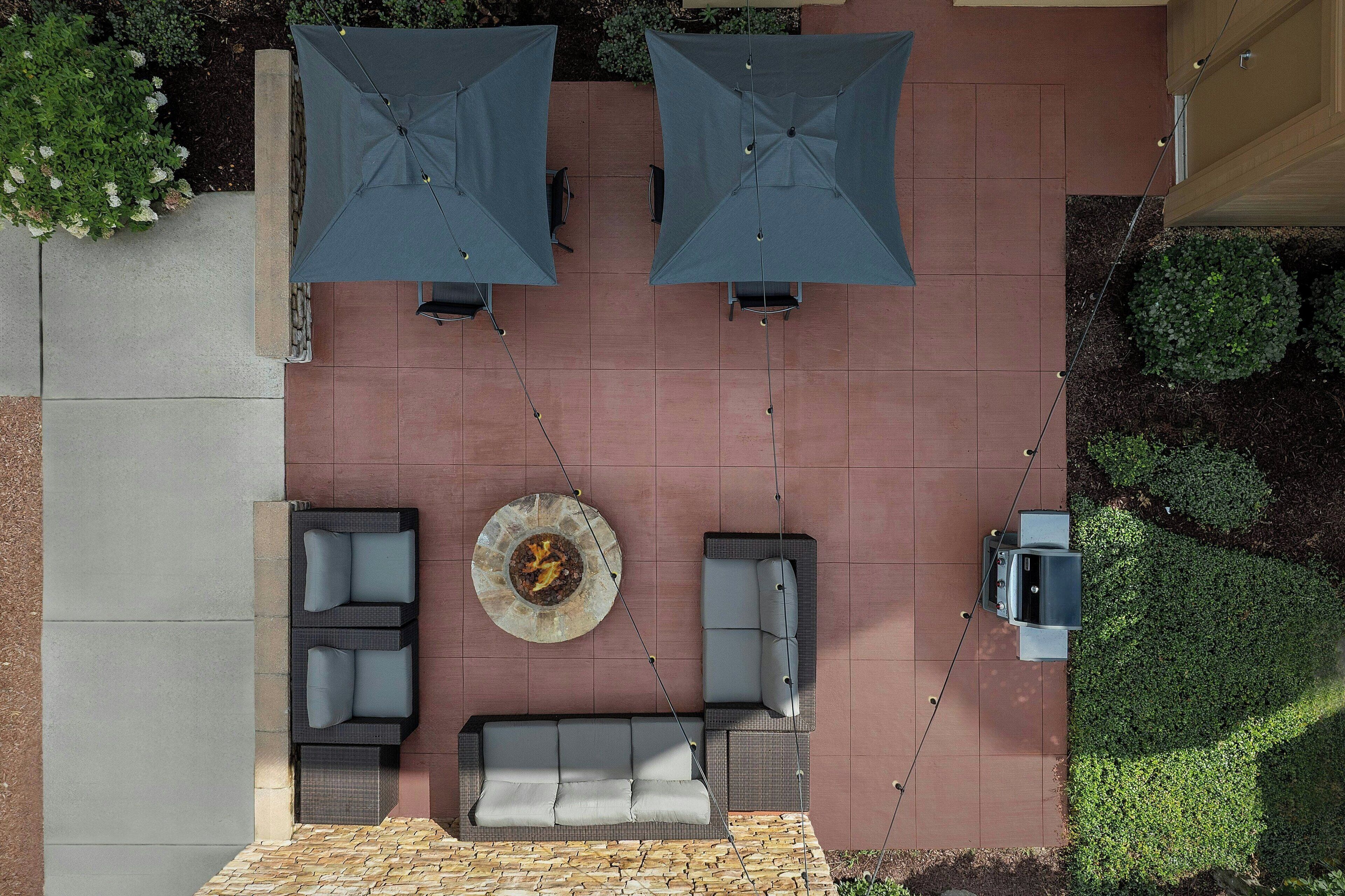 A patio with two umbrellas, a fire pit, and a sofa.
