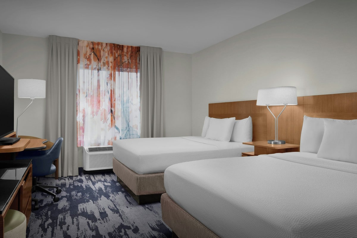 Une chambre d’hôtel avec deux lits, un bureau avec une chaise, une télévision et une fenêtre avec des rideaux.