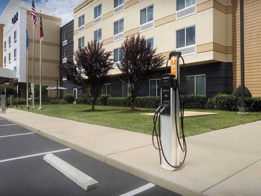 A hotel with a parking lot, EV charging station, and a flagpole with flags.