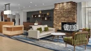 A modern lobby with a reception desk, a sofa, a chair, a fireplace, and a decorative wall. - Fairfield Inn & Suites by Marriott Fayetteville North (Fayetteville)
