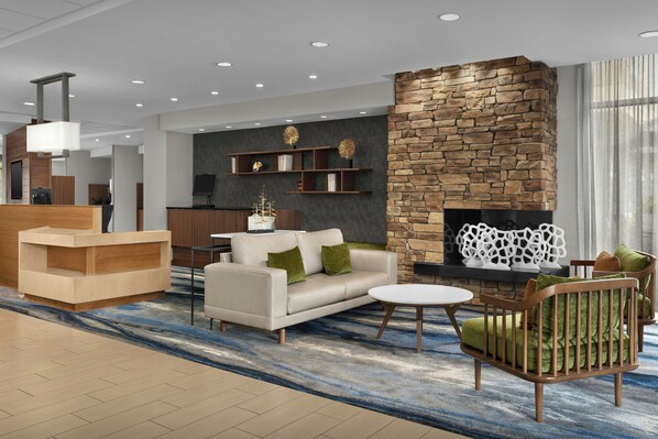 A modern lobby with a reception desk, a sofa, a chair, a fireplace, and a decorative wall. - Fairfield Inn & Suites by Marriott Fayetteville North (Fayetteville)