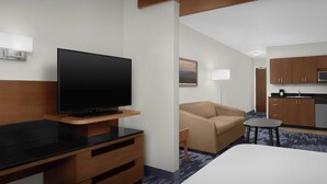 A modern hotel room with a flat-screen TV, wooden desk, beige sofa, and a small table. - Fairfield Inn & Suites by Marriott Fayetteville North (Fayetteville)