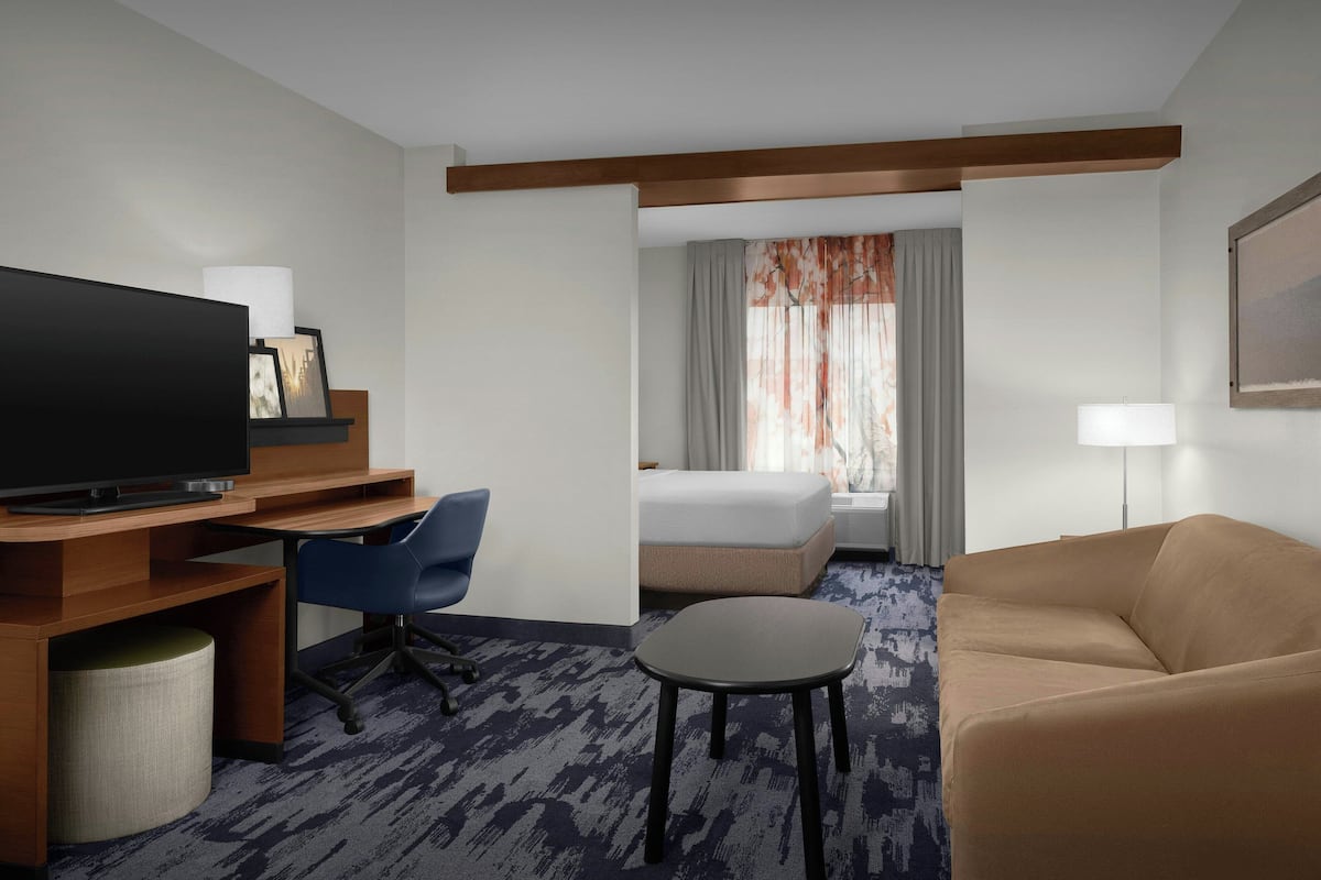 Une chambre d’hôtel comprenant un lit, une télévision, un bureau avec une chaise, une petite table et un canapé.