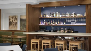 A bar area with wooden shelves stocked with bottles and glasses, a cash register, and a seating area with tables and chairs. - Fairfield Inn & Suites by Marriott Fayetteville North (Fayetteville)