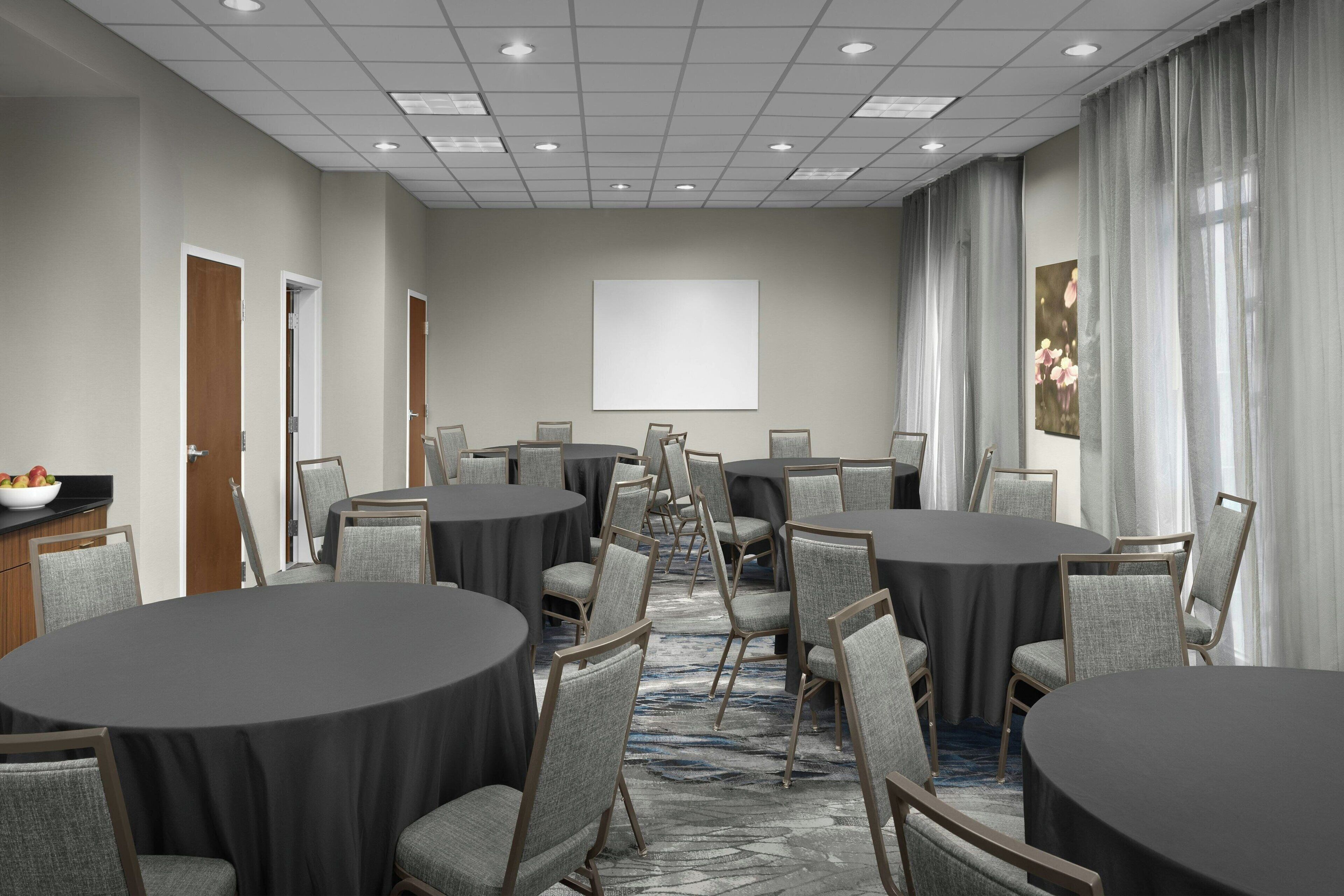 A conference room with round tables and chairs, a projector screen, and a carpeted floor.