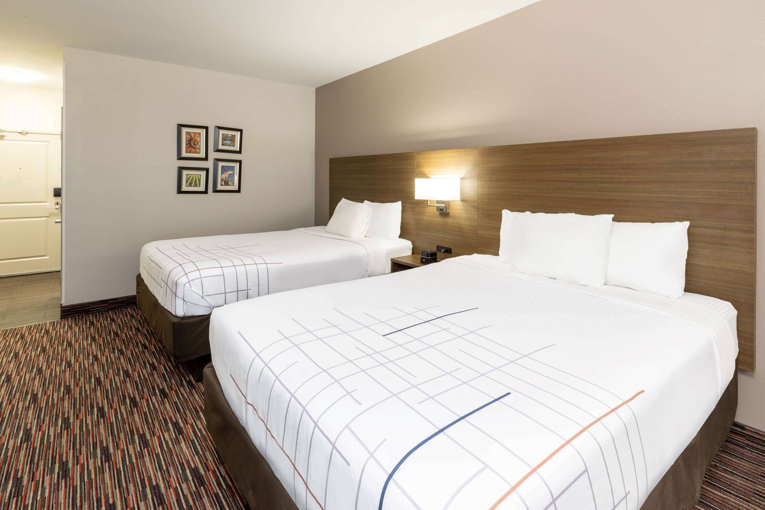 A hotel room with two beds, a headboard with a light fixture, and a carpeted floor.