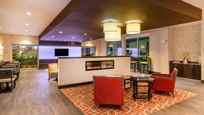 A hotel lobby with a reception desk, seating area, and a large window with a view of the parking area.