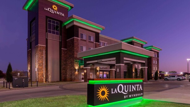 A hotel with a prominent sign reading "LA QUINTA BY WYNDHAM" and a modern architectural design with green lighting accents.