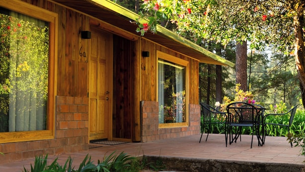 Une cabane en bois avec une entrée en briques, de grandes fenêtres et une terrasse aménagée avec du mobilier d’extérieur.