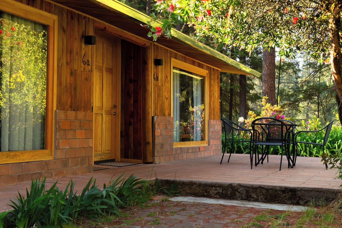 A wooden cabin with a brick entrance, large windows, and a patio with outdoor furniture.