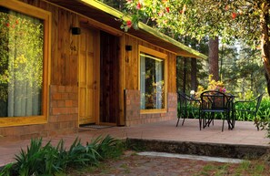 A wooden cabin with a brick entrance, large windows, and a patio with outdoor furniture.