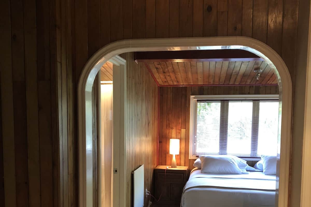 A wooden room with a bed, a lamp, and a window.