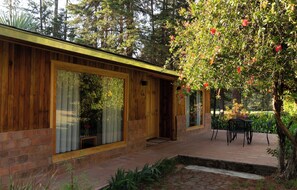 A wooden cabin with large windows, a brick exterior, and a patio with a table and chairs.