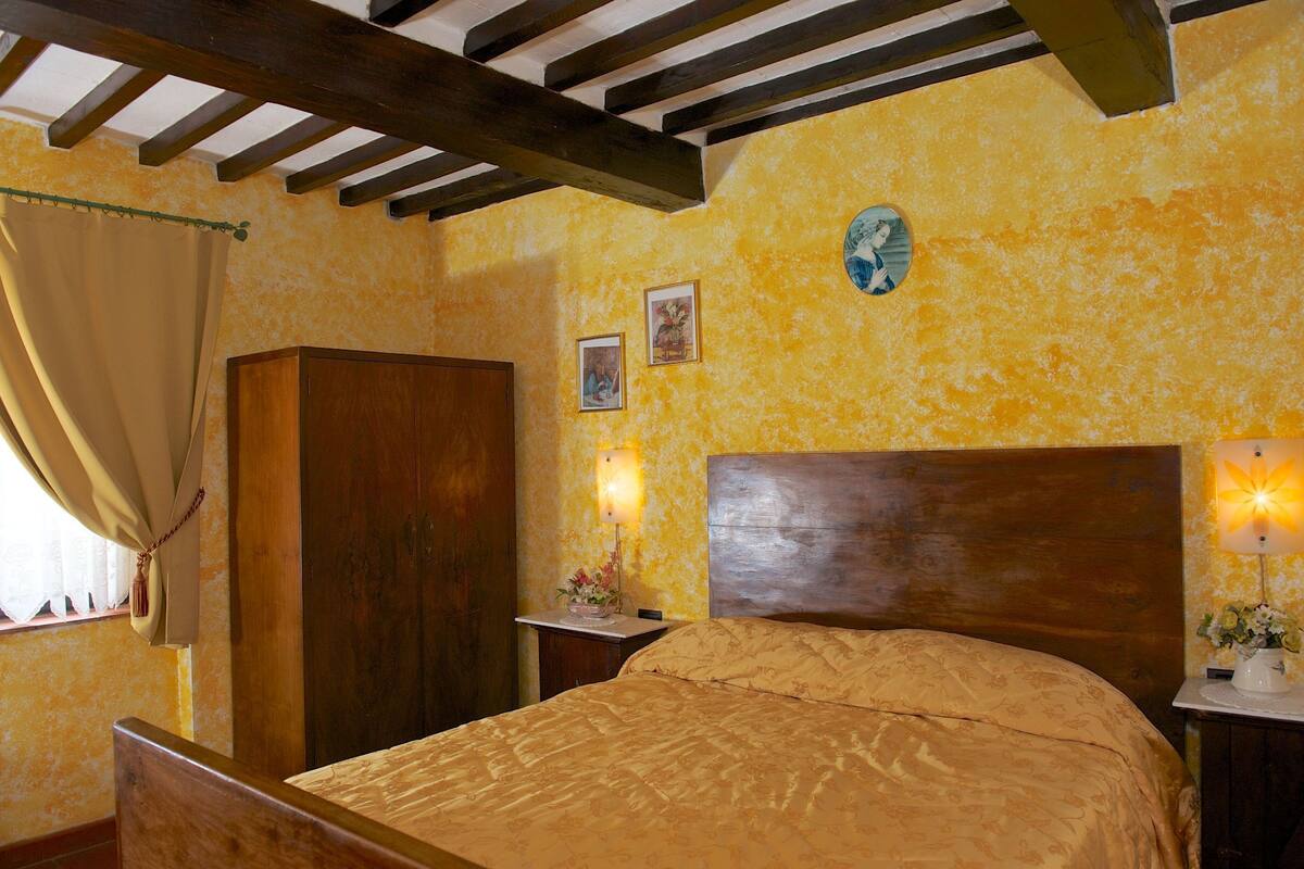 Ein Schlafzimmer mit einem hölzernen Kopfteil, einem Bett mit einem gemusterten Bettbezug, einem Nachttisch mit Lampe und einem Holzschrank.