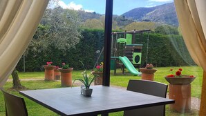 Een eethoek met een tafel en stoelen, uitzicht op een speeltuin en potplanten.