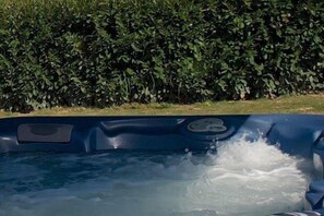 A hot tub with water splashing, surrounded by a hedge.