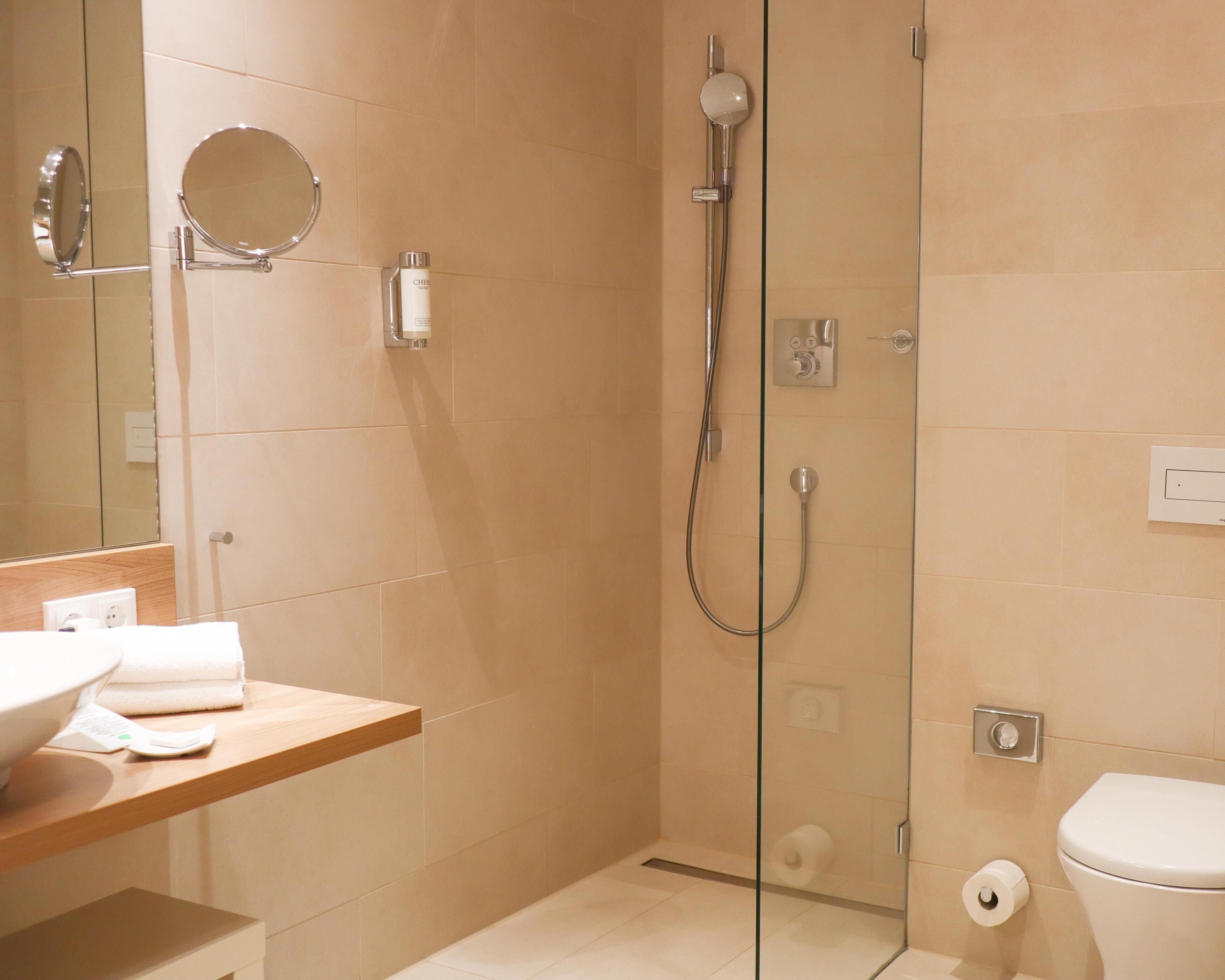 Une salle de bain moderne avec une douche à parois de verre, un miroir rond, un lavabo avec un plan de travail et des toilettes.