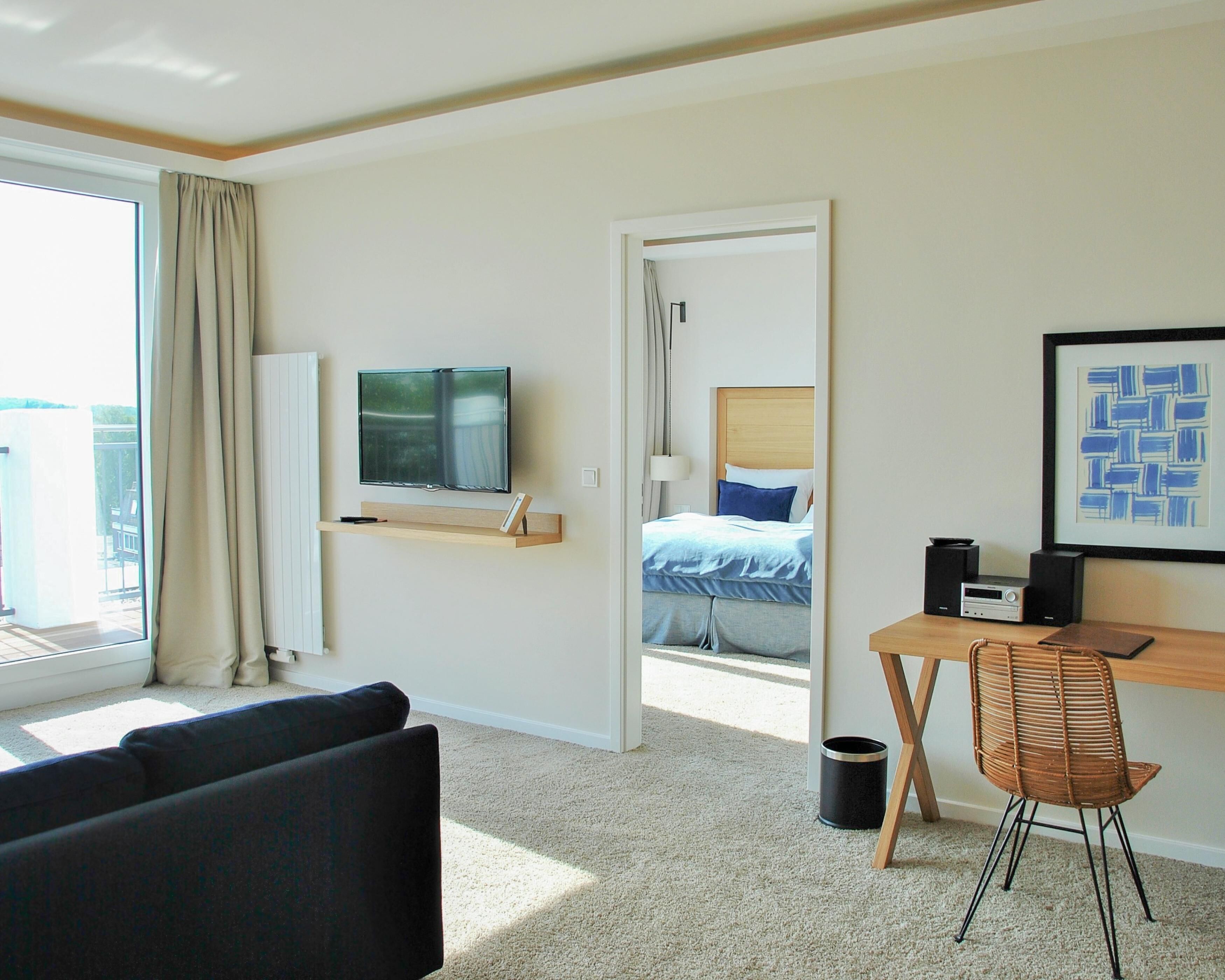 Quarto de hotel com cama, televisão, escrivaninha com cadeira e janela com cortinas.