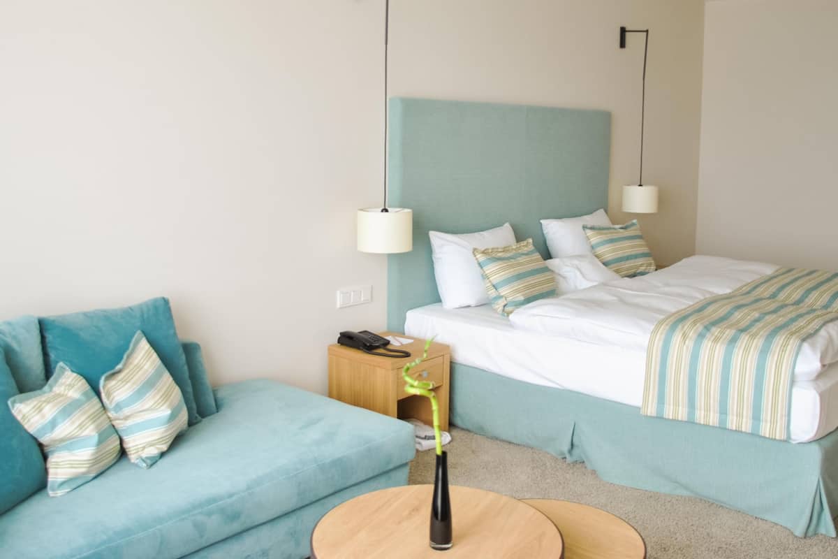 Ein Hotelzimmer mit einem Bett, einem blauen Sofa, einem Nachttisch mit Lampe und einem kleinen Tisch mit einer Vase.