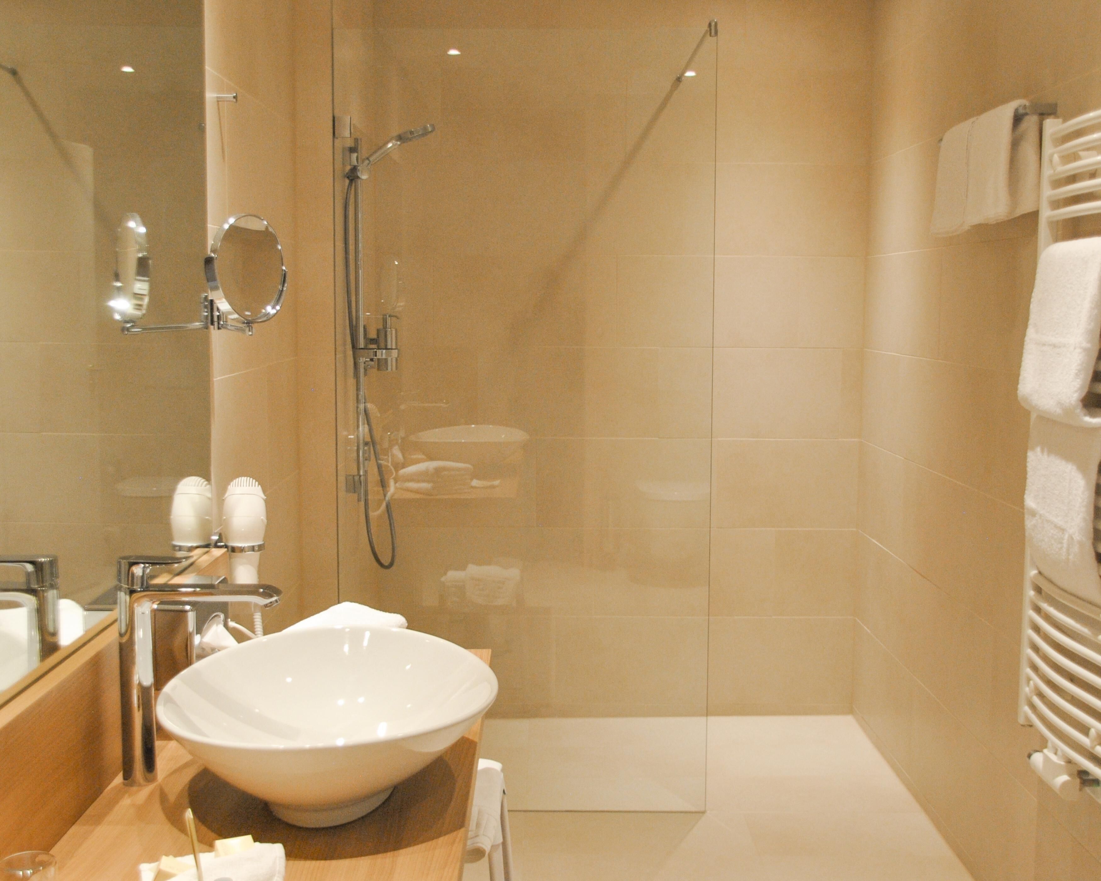 A modern bathroom with a large white sink, a glass-enclosed shower, and a towel rack with multiple towels.