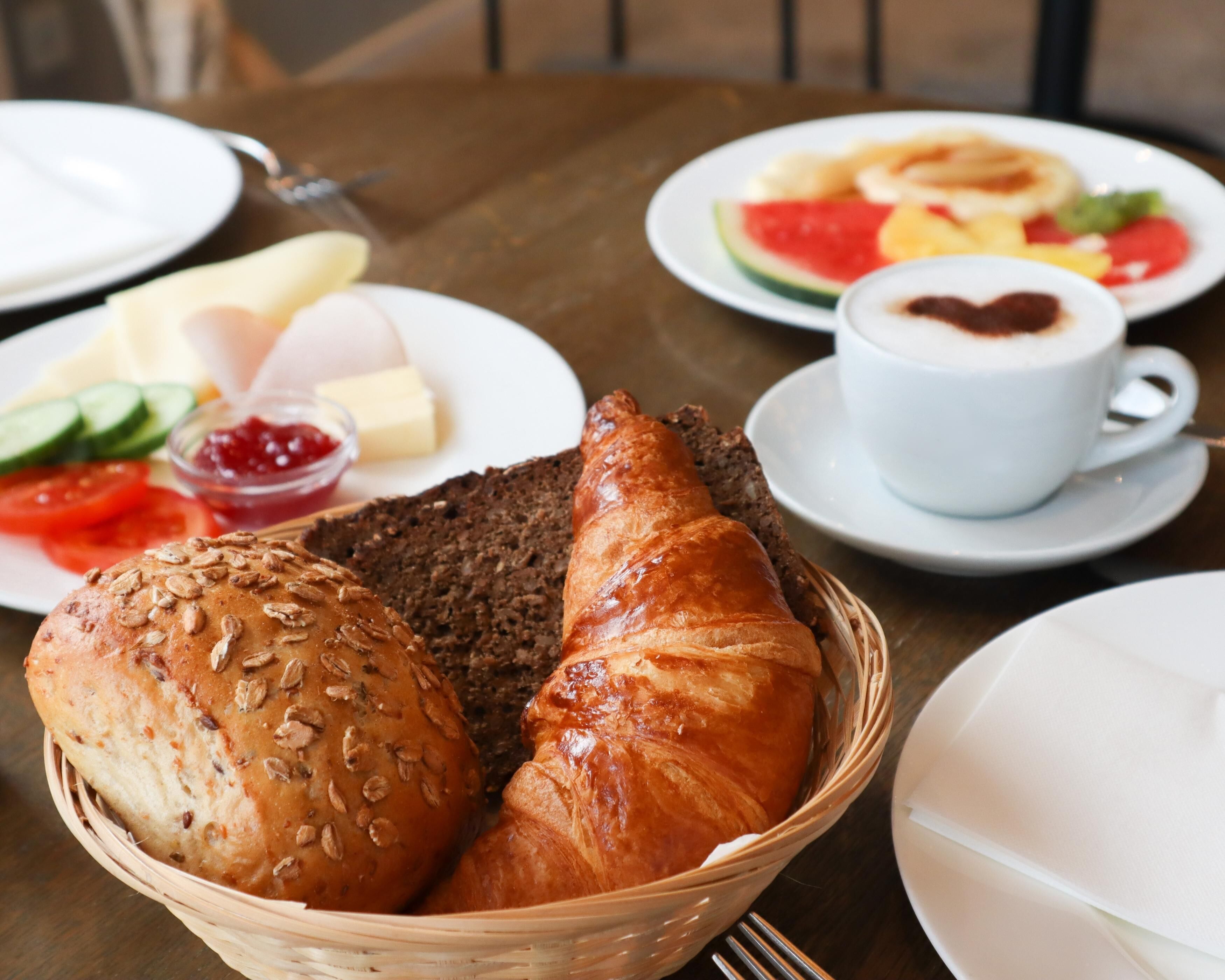 A breakfast setting with bread, croissants, and a cup of coffee on a table.