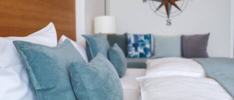 A neatly made bed with teal and white pillows, a wooden headboard, and a compass wall decoration.
