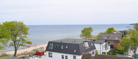 A residential area with a view of the sea, featuring houses with various roof styles and a beach in the background.