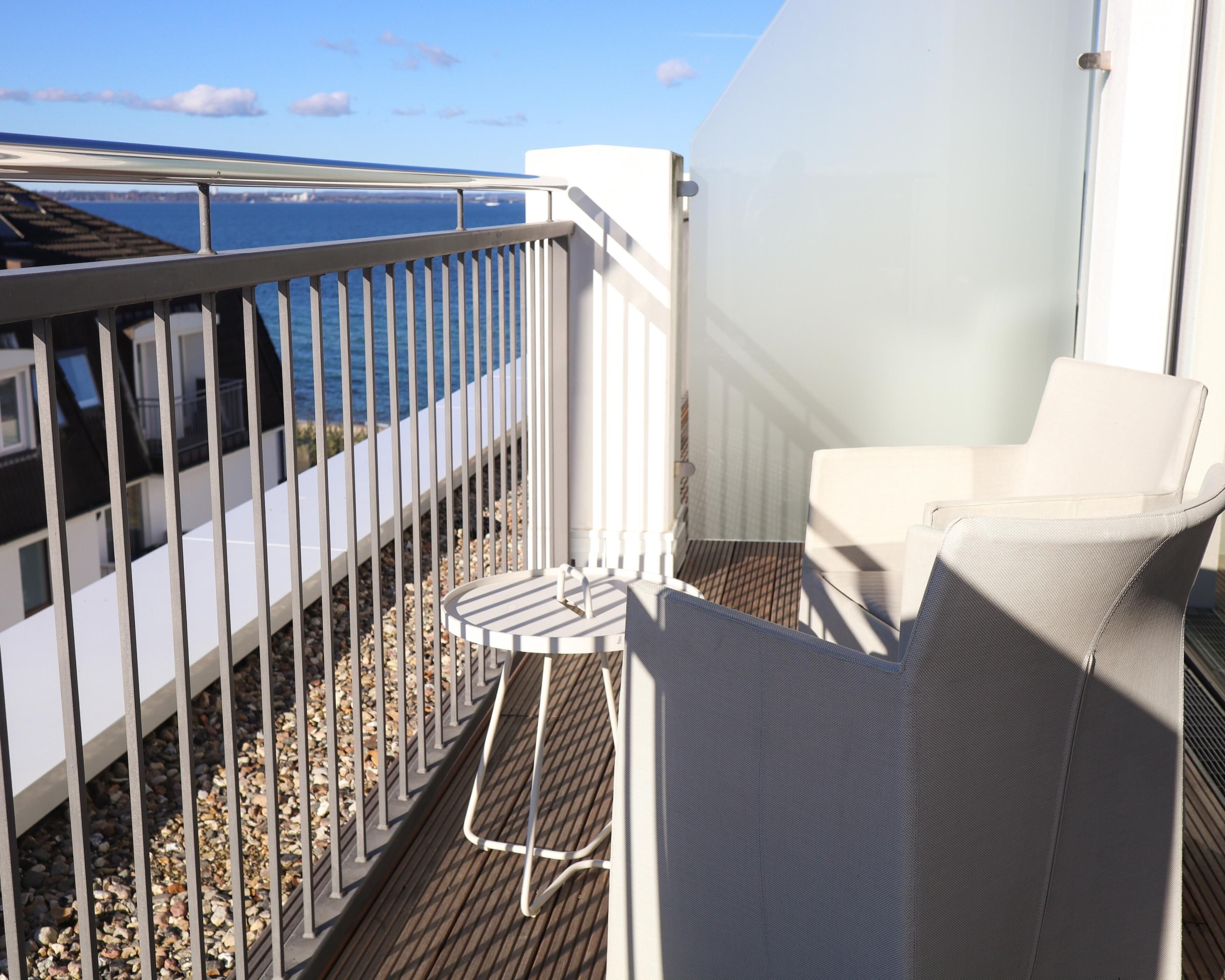 Un balcone con ringhiera bianca, un tavolino rotondo e una sedia bianca. Il balcone si affaccia su un corpo d'acqua.