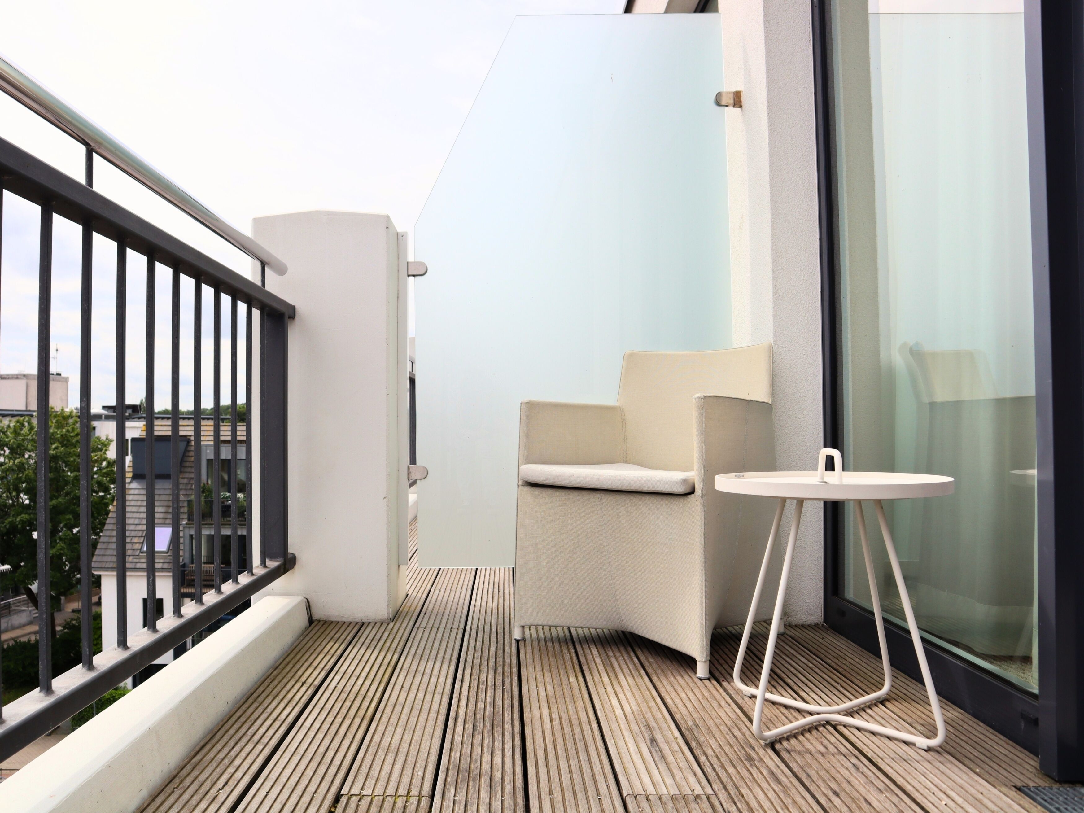 A balcony with a wooden floor, a white chair, a small round table, and a glass door.