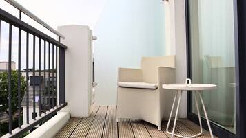 A balcony with a wooden floor, a white chair, a small round table, and a glass door.